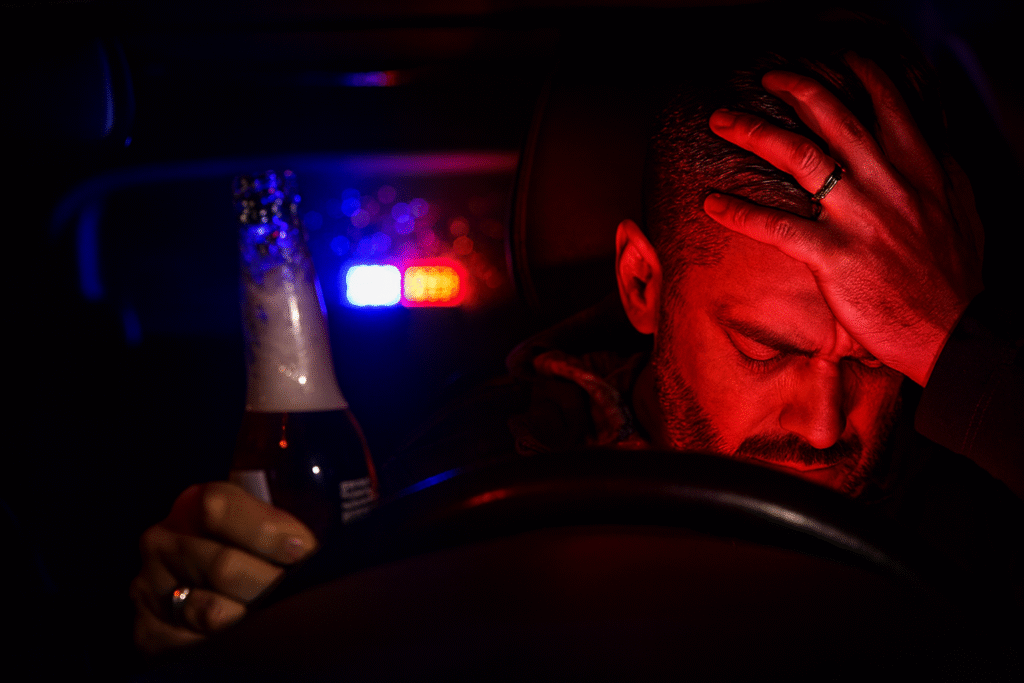 A distressed man with a wedding ring holding a beer bottle in his car, lit by police sirens, symbolizing the dangers and penalties of exceeding the Ontario alcohol limit for driving.